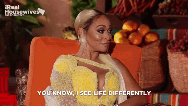 a woman in a yellow dress is sitting in an orange chair and saying " you know i see life differently "