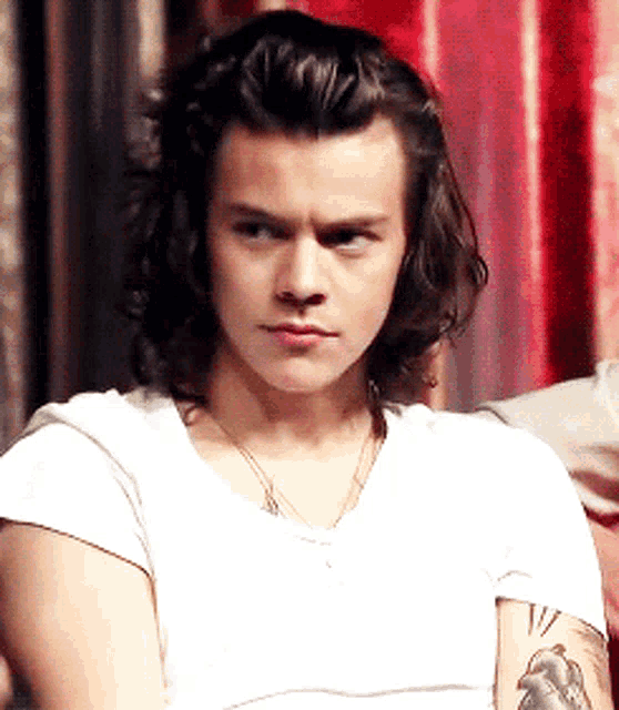 a young man with long hair is wearing a white shirt and has a tattoo of a heart on his arm