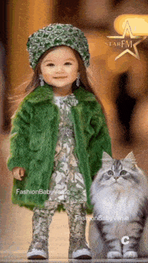 a little girl in a green fur coat is standing next to a cat in a star fm photo