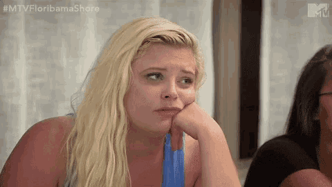 a blonde woman is sitting at a table with her hand on her chin and a sad look on her face .