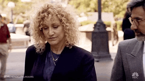 a woman with curly hair is standing next to a man with glasses .
