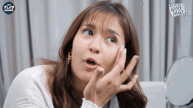 a woman is looking at her face in front of a mirror with a play advertisement on the bottom