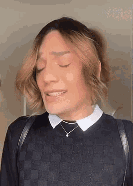 a man wearing a black sweater and a white collar is making a funny face with his eyes closed .