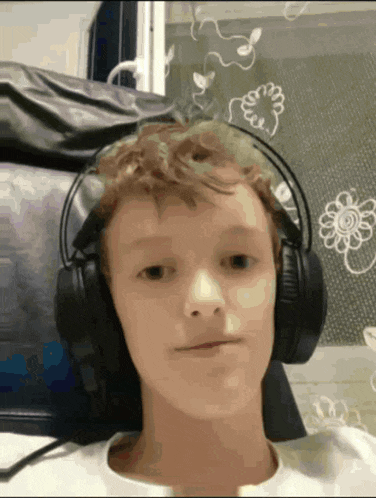 a young boy wearing headphones looks at the camera with a flower in the background