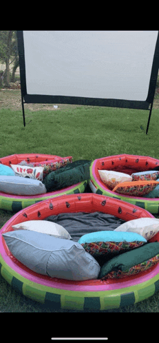 a row of watermelon shaped pools filled with pillows and blankets in front of a screen .