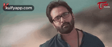a man with a beard and glasses is standing in front of a blue sky .