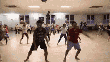a group of people are dancing in a room with a man wearing a batman shirt on