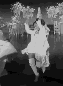 a black and white photo of a woman dancing on a dance floor at a wedding .