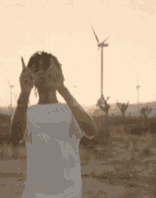 a man in a white shirt is standing in front of a windmill in the desert .