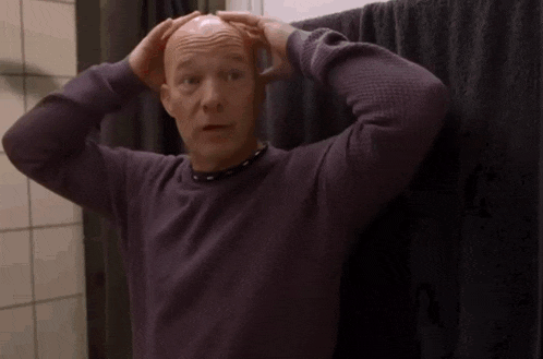a bald man in a purple shirt is standing in front of a towel .