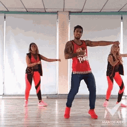 a man in a red tank top is dancing with two women in a gym .