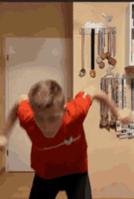 a boy in a red shirt is dancing in front of a wall with medals on it
