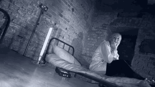 a woman is sitting on a bed in front of a brick wall with a sign that says exit
