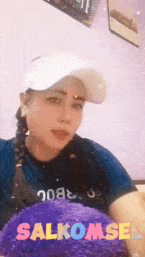 a woman wearing a hat is holding a purple pillow with salkomsel written on it