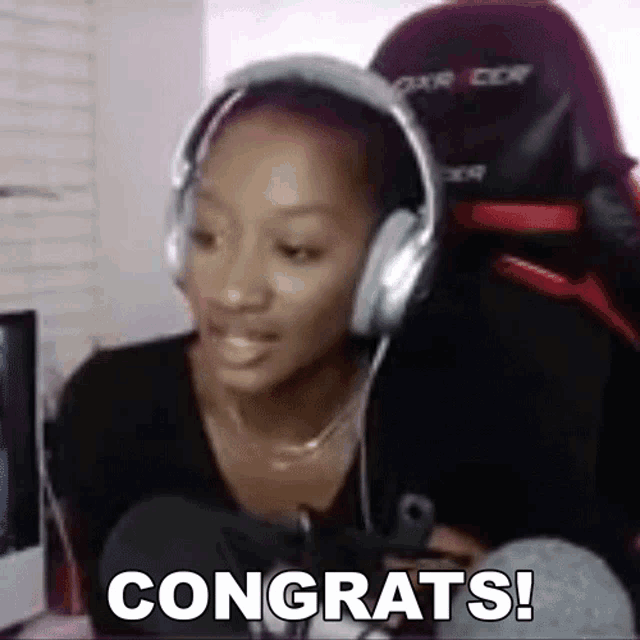 a woman wearing headphones is sitting in front of a computer and says congrats .