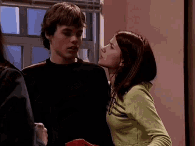 a man and a woman are standing next to each other in a room . the woman is wearing a green sweatshirt .