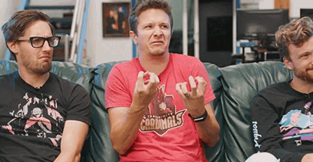 three men are sitting on a couch and one of them is wearing a red shirt that says cardinals