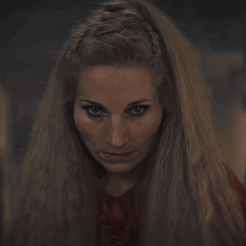 a woman with long blonde hair and a braided headband looks at the camera