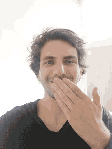 a man covering his mouth with his hands in a black shirt