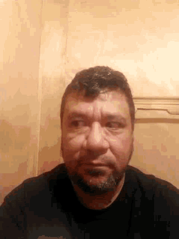 a man with a beard is making a funny face while standing in front of a wooden wall .