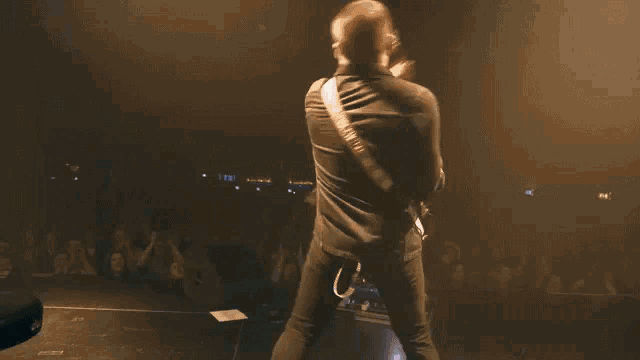a man is playing a guitar on stage in front of a crowd with a sign that says g on it