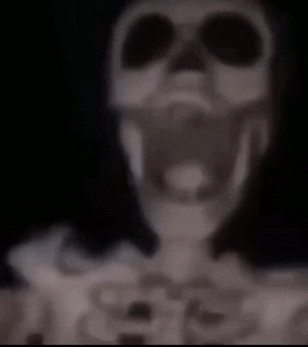 a blurry picture of a skeleton with its mouth open and a black background .