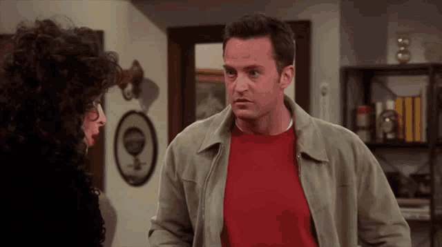a man in a red shirt is talking to a woman in a room