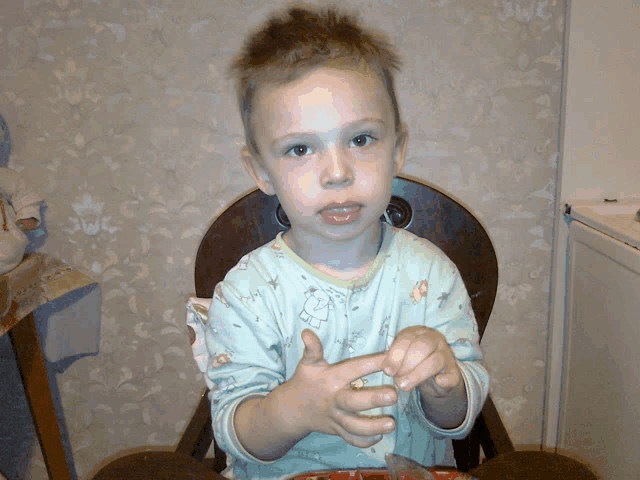 a young boy sitting in a high chair with his hands in his pockets