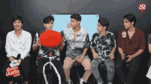 a group of young men are sitting in front of a tv with the letters s on the screen