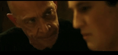 two men are looking at each other in a dark room and one of them is making a funny face .