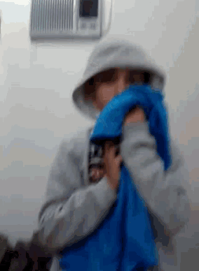 a person wearing a grey hoodie is holding a blue shirt in front of their face ..