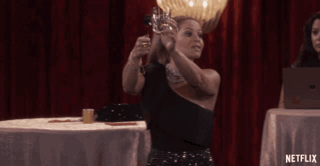 a woman holds a glass in front of a red curtain with netflix written on the bottom
