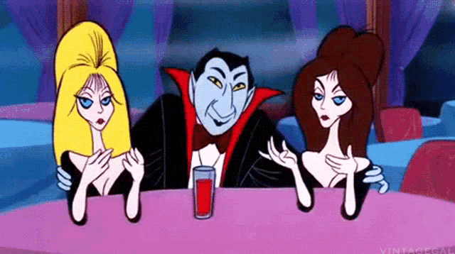 a vampire and two women are sitting at a table with a glass of blood .