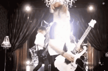 a man is playing a white electric guitar on a stage in front of a chandelier .