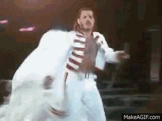 a man in a white suit is dancing on a stage with a makeagif.com watermark