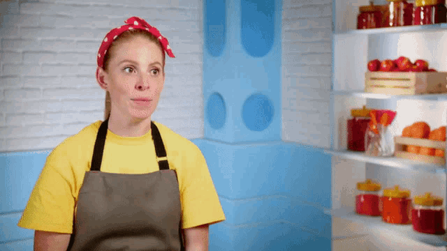a woman wearing an apron and a yellow shirt stands in front of a shelf full of jars