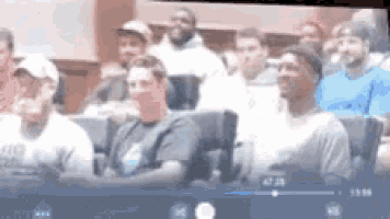 a group of men are sitting in a classroom watching a video on a tv screen .