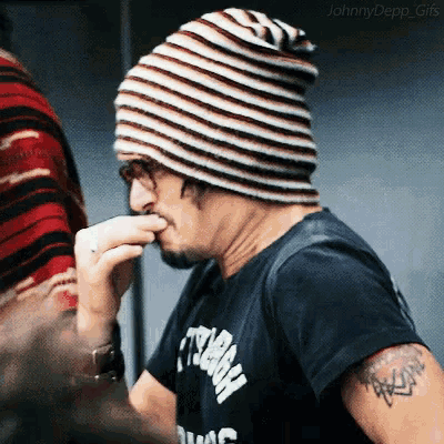 a man wearing a striped beanie and a black shirt with a tattoo on his arm is eating something