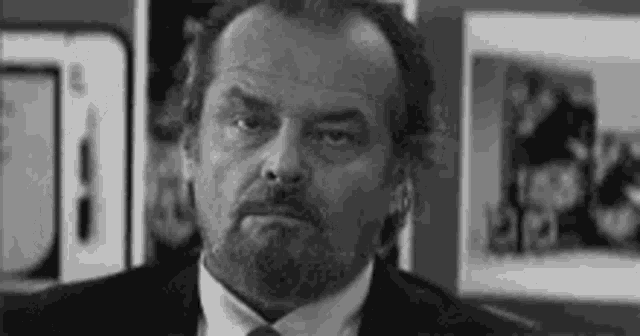 a black and white photo of a man in a suit and tie looking at the camera .