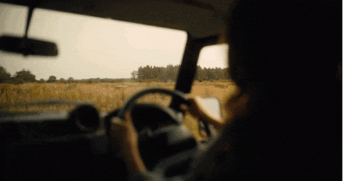 a person is driving a car on a dirt road with a field in the background .