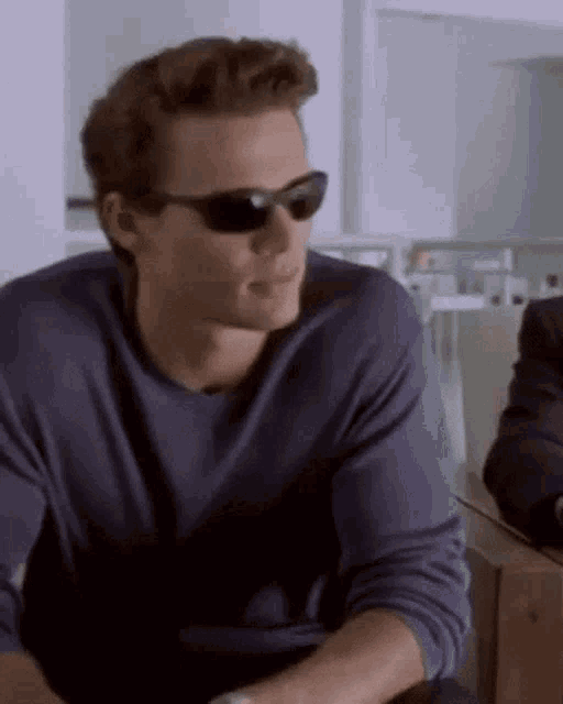 a man wearing sunglasses and a blue shirt is sitting at a table