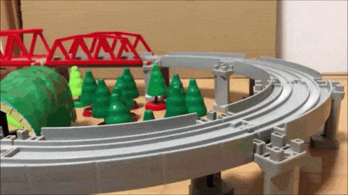 a toy train track with trees and a bridge in the background