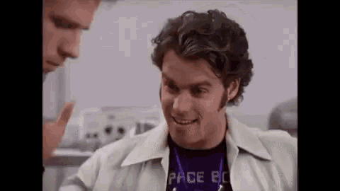 a man wearing a purple shirt and a lanyard is talking to another man in a room .