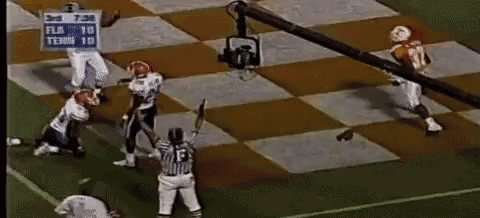 a group of football players are playing a game on a checkered field with a referee in the middle .