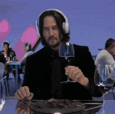 a man wearing headphones is sitting at a table holding a glass of wine