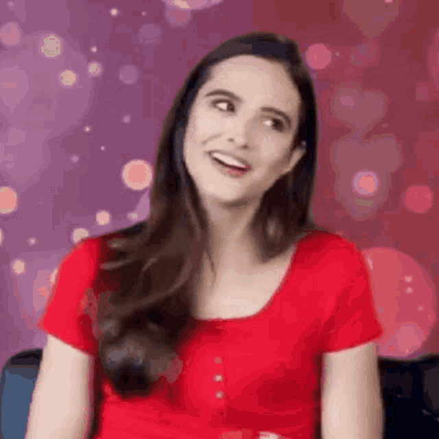 a woman in a red shirt is smiling and looking to the side .