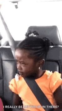 a little girl is sitting in the back seat of a car and making a funny face .