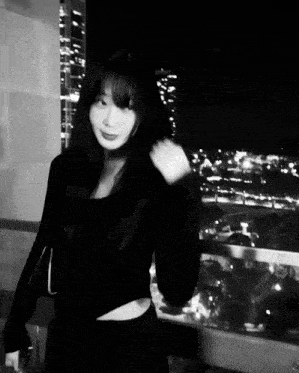 a black and white photo of a woman standing on a balcony at night