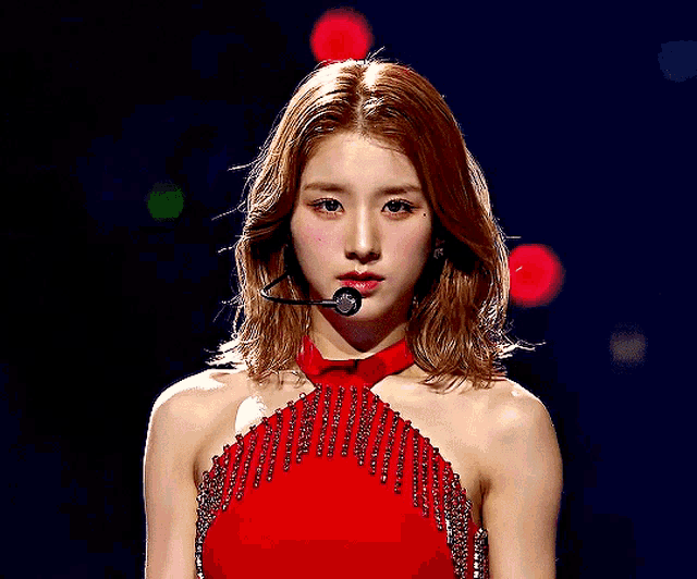 a woman in a red dress is wearing a microphone and looking at the camera