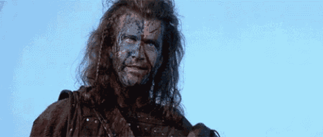 a man with long hair and blue paint on his face is holding a sword .
